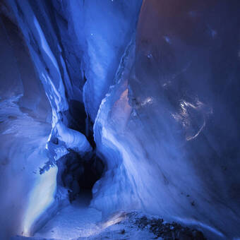 Blick in eine beleuchtete blaue Eishöhle 